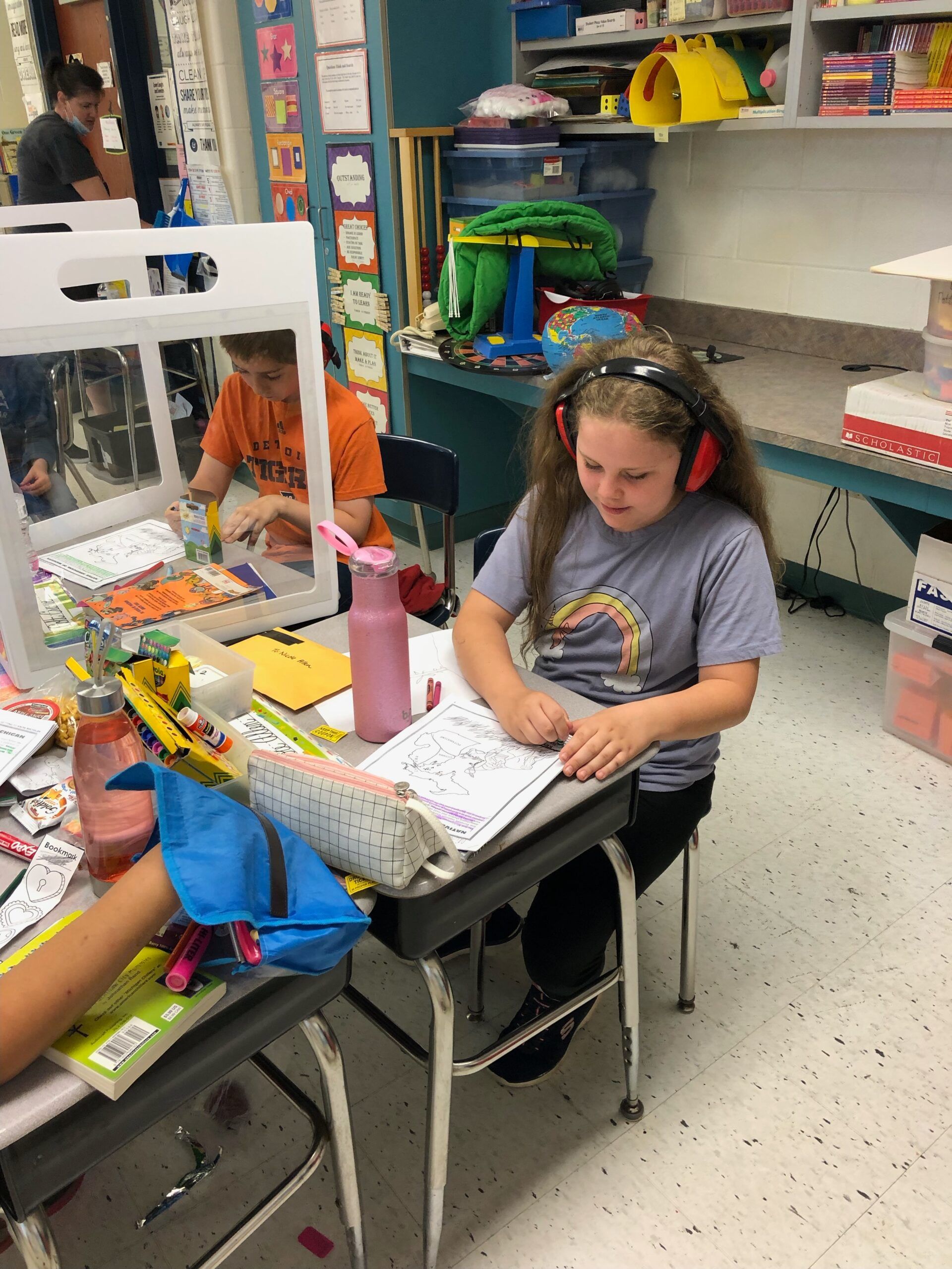A girl wearing headphones sits at a desk in a classroom.