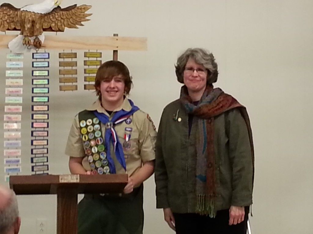 A boy scout is standing next to a woman.
