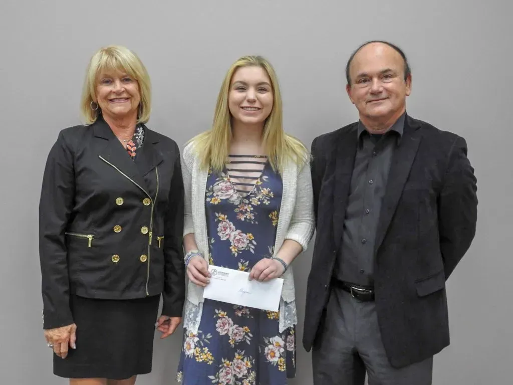 A woman holding a check standing next to two adults.
