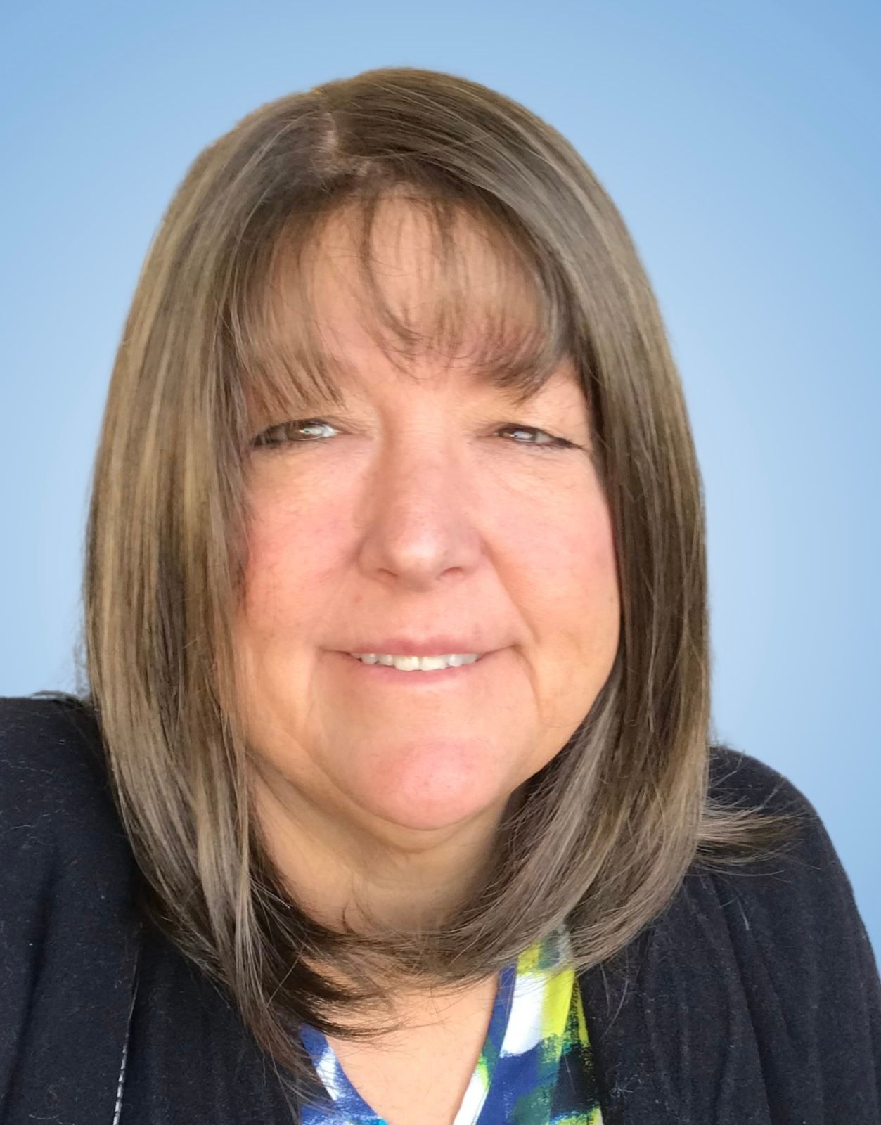A woman with brown hair and a blue shirt is smiling for the camera.