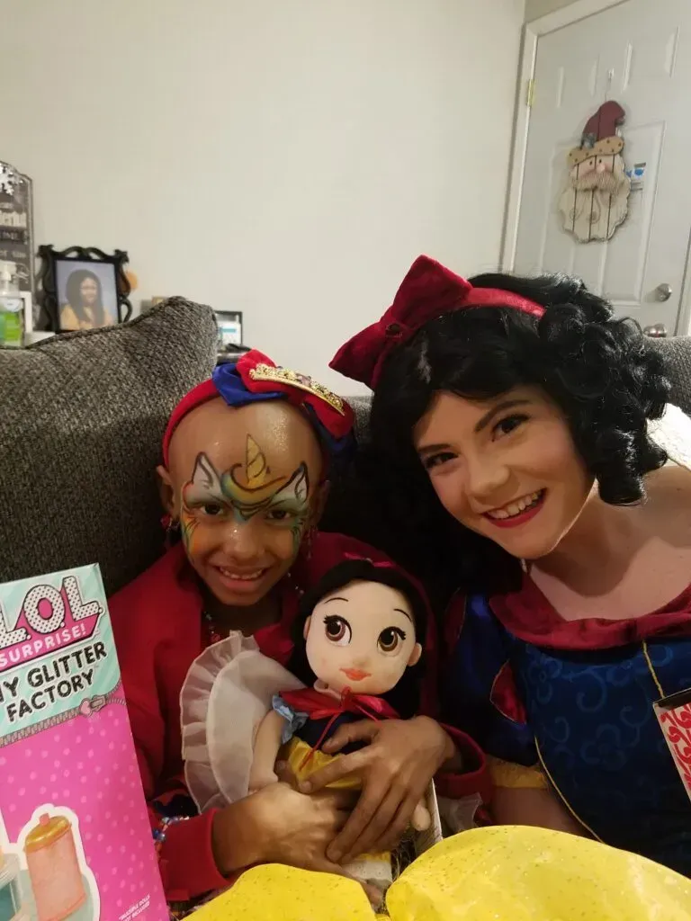 A woman dressed as Snow White and a kid with a Snow White doll are smiling for a picture.
