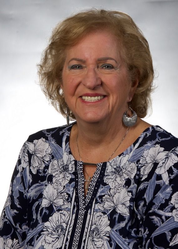 A woman in a blue and white floral shirt is smiling for the camera.