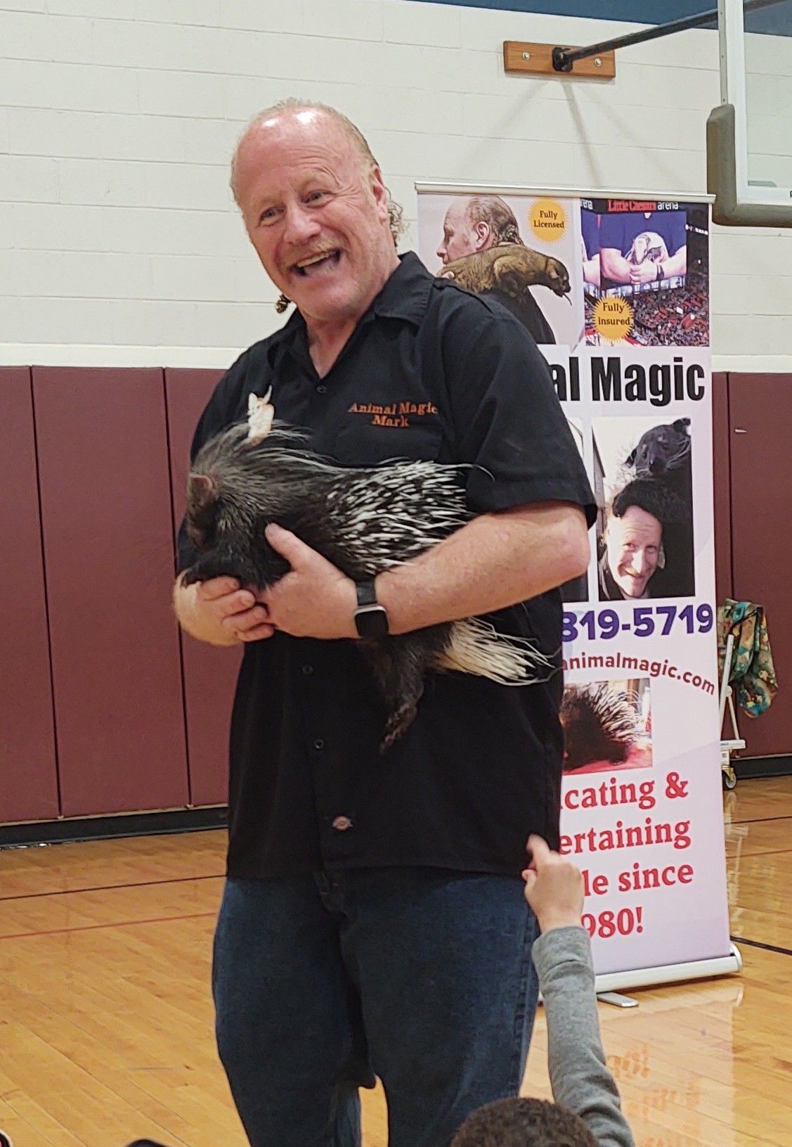 A man holding a porcupine in front of a sign that says animal magic.