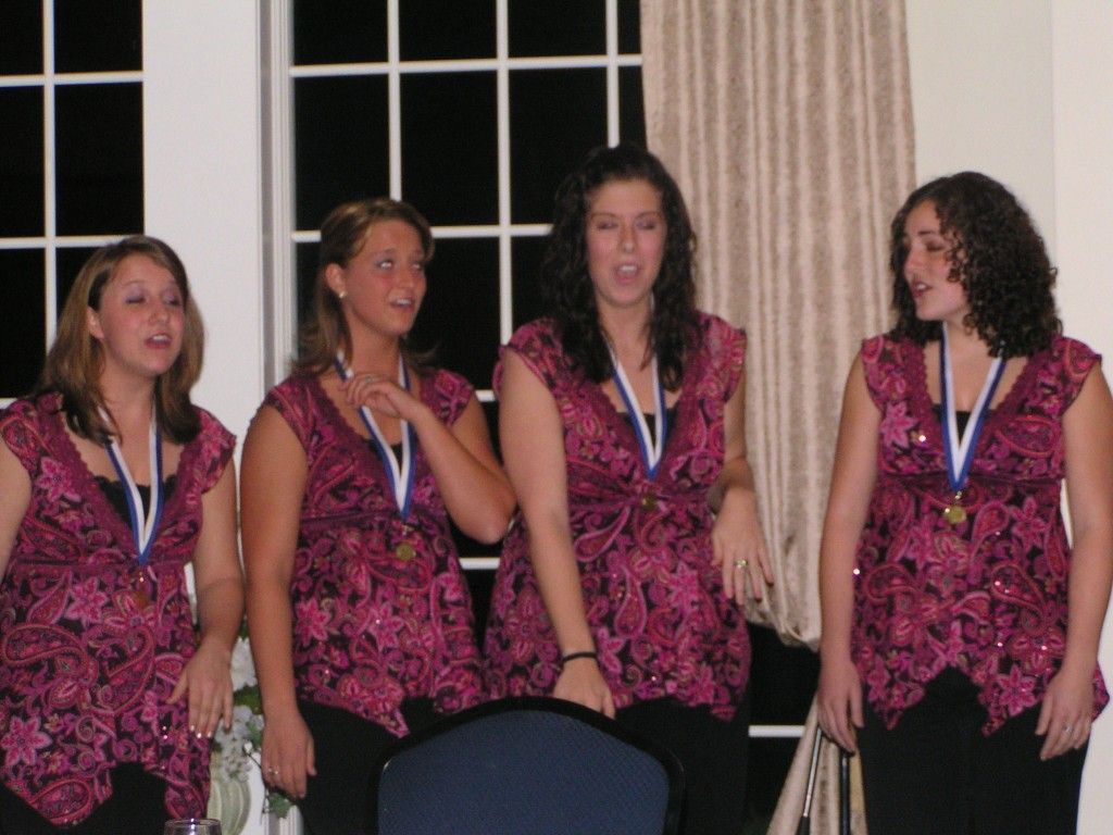 A group of young women wearing medals stand in front of a window.