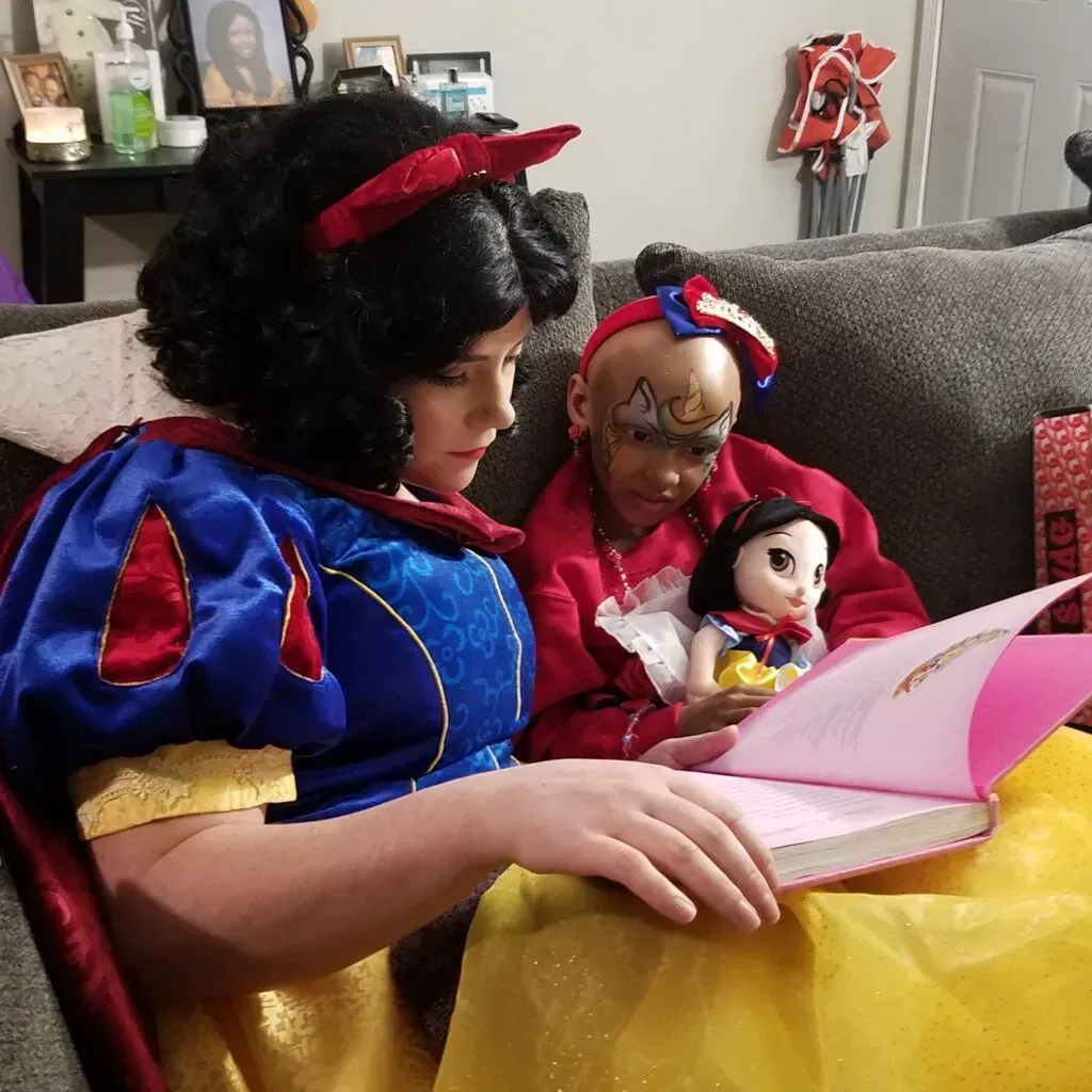 A woman dressed as Snow White is reading to a kid with a Snow White doll.