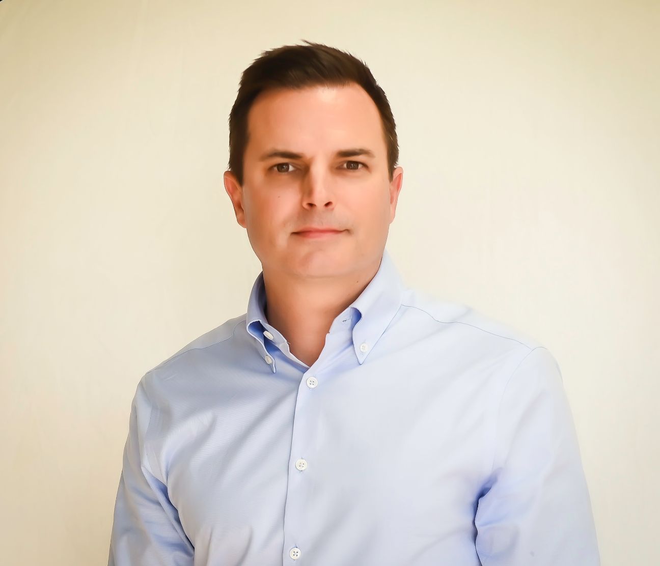 A man in a blue shirt is standing in front of a white wall