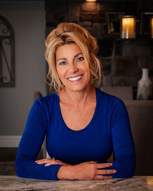 A woman in a blue shirt is sitting at a table with her hands folded