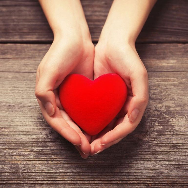 A person is holding a red heart in their hands.