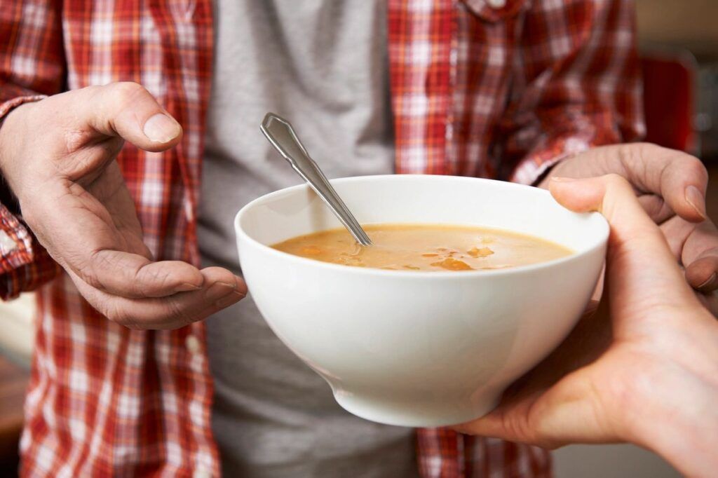 A person is holding a bowl of soup with a spoon in it.