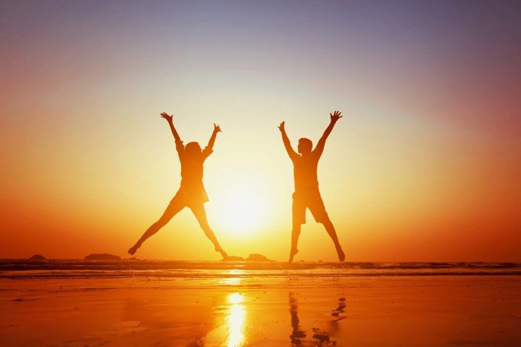 Two people jumping in the air on a beach at sunset.