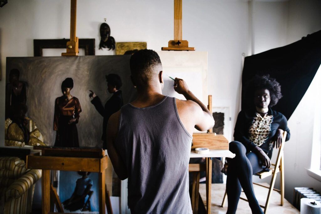 A man is painting a picture of a woman sitting in a chair.