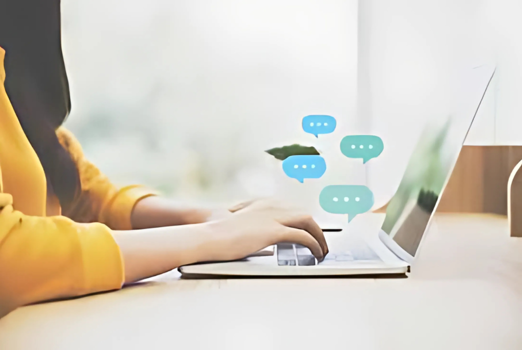 A woman is typing on a laptop computer with speech bubbles on the screen.