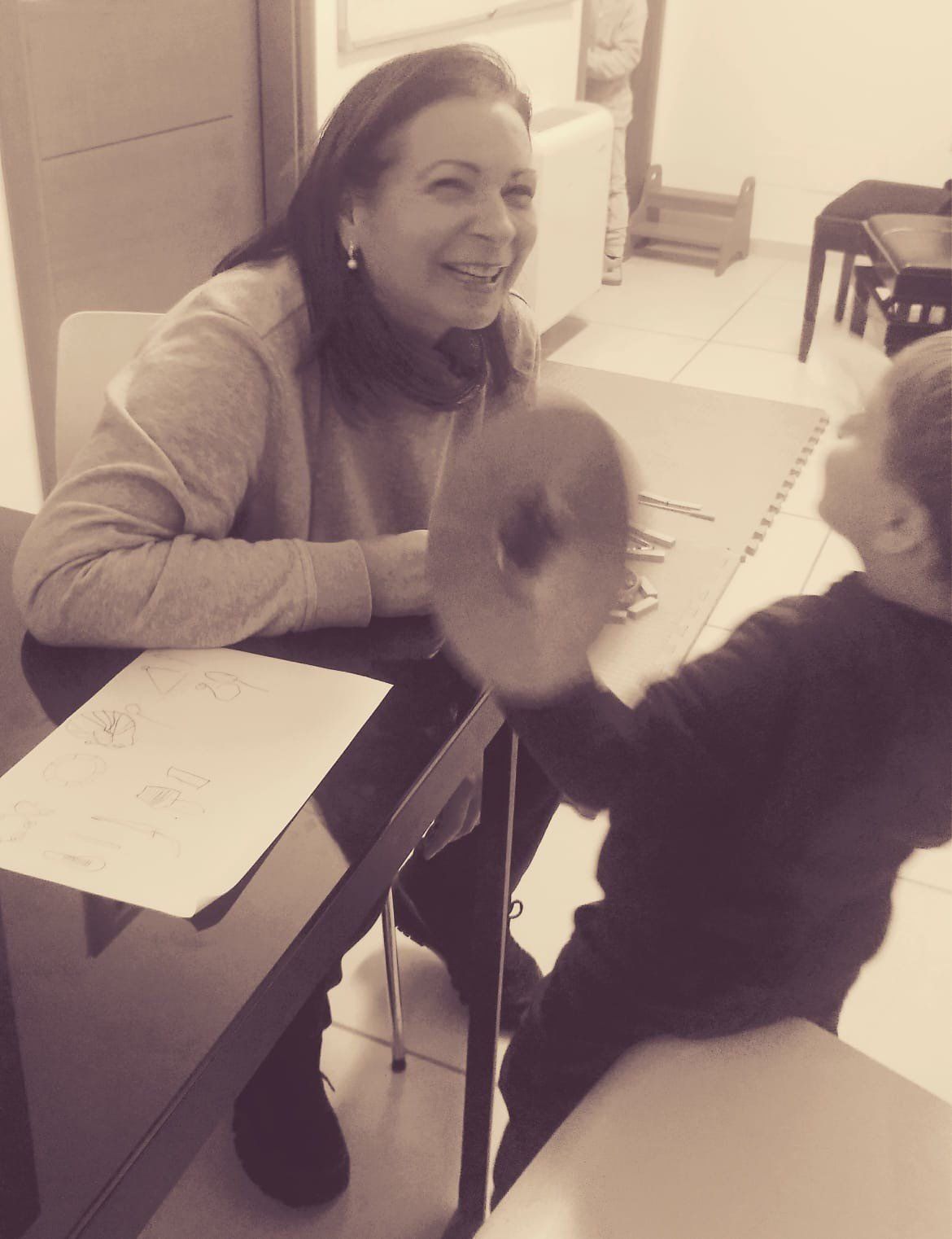 La donna ride mentre il bambino solleva un oggetto rotondo su un tavolo.