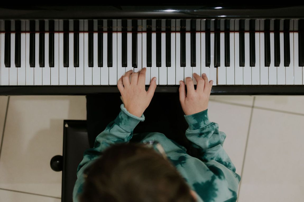 Mani che suonano i tasti del pianoforte; bambino con maglione verde seduto allo strumento.