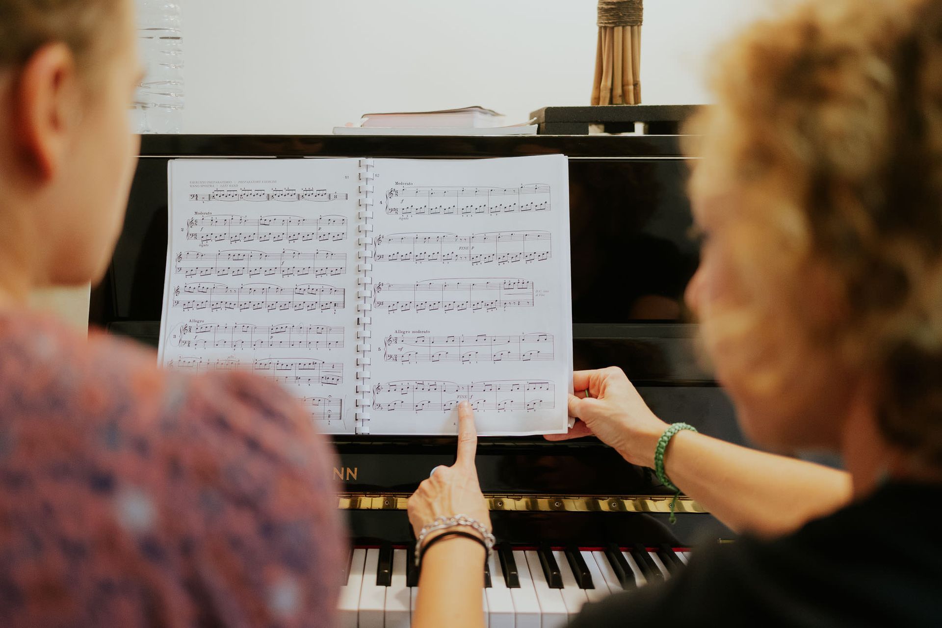 Due persone guardano uno spartito su un pianoforte, una delle quali indica la pagina.