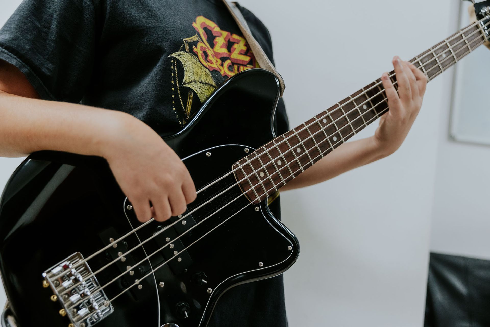 Persona che suona una chitarra elettrica bianca a forma di V, in primo piano. Indossa una maglietta nera e una tracolla per chitarra.