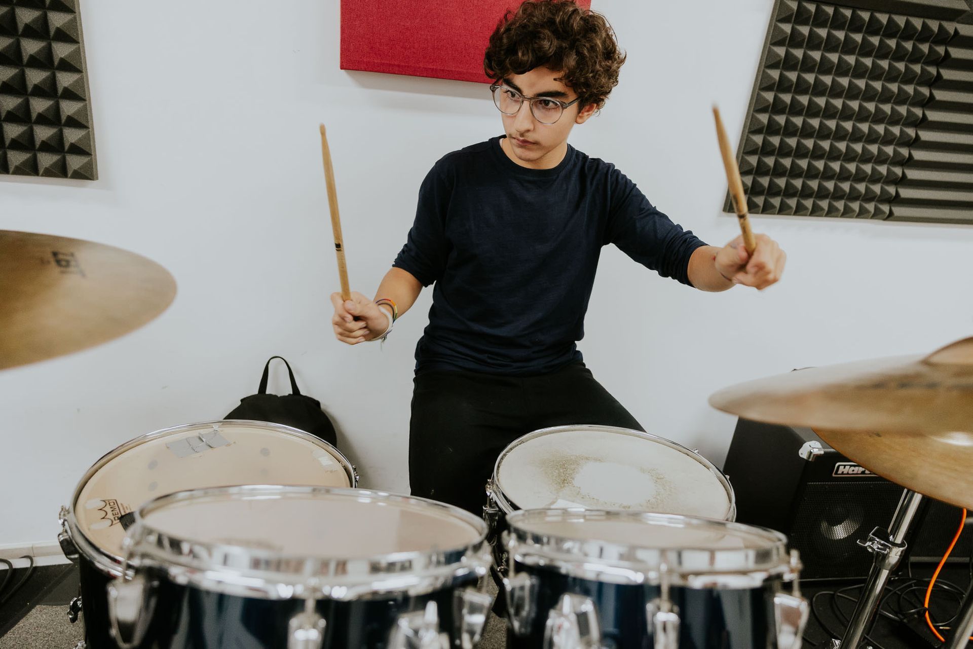 Una persona suona la batteria in uno studio, colpendo i piatti con bacchette di legno.