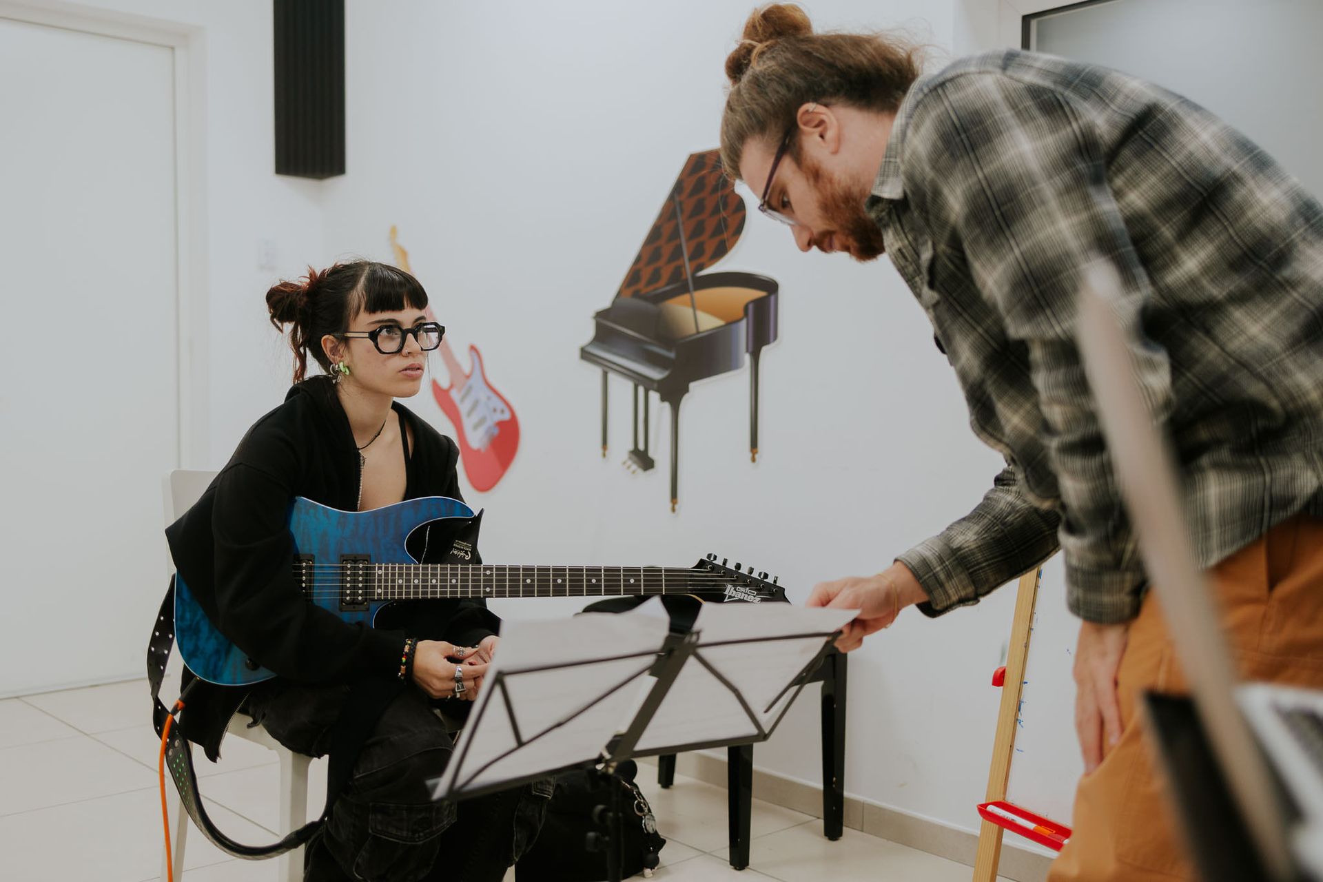 Studente e insegnante di chitarra che guardano gli spartiti in una sala musica.