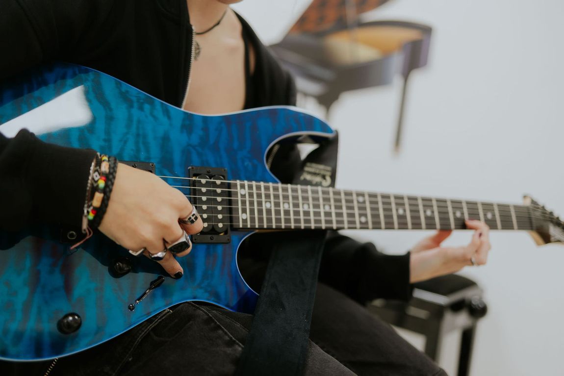 Persona che suona una chitarra elettrica blu, dita sulla tastiera. Vestito nero, smalto nero.