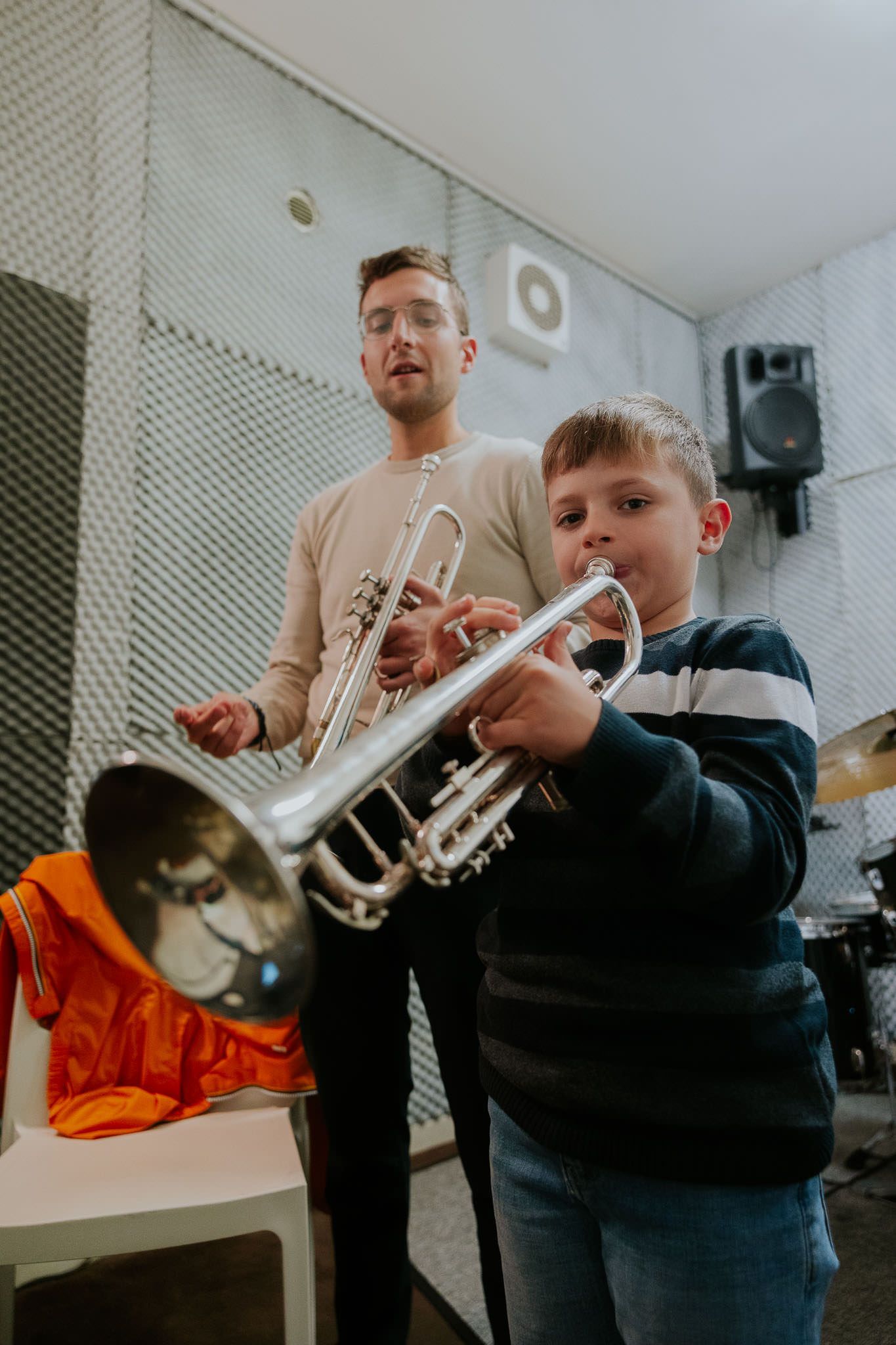 Un uomo e un ragazzo suonano la tromba in uno studio musicale. Il ragazzo è concentrato e soffia nello strumento.