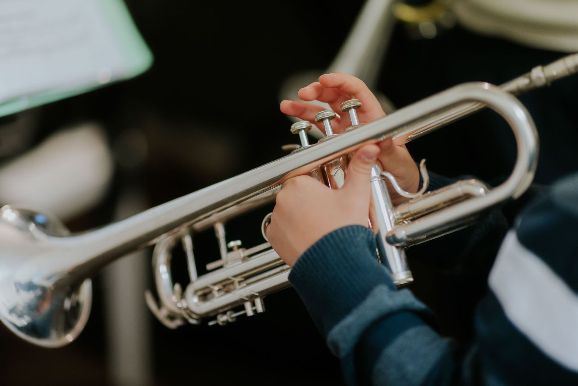 Persona che suona una tromba d'argento, con le mani sui pistoni, e indossa una camicia a righe blu e bianche.