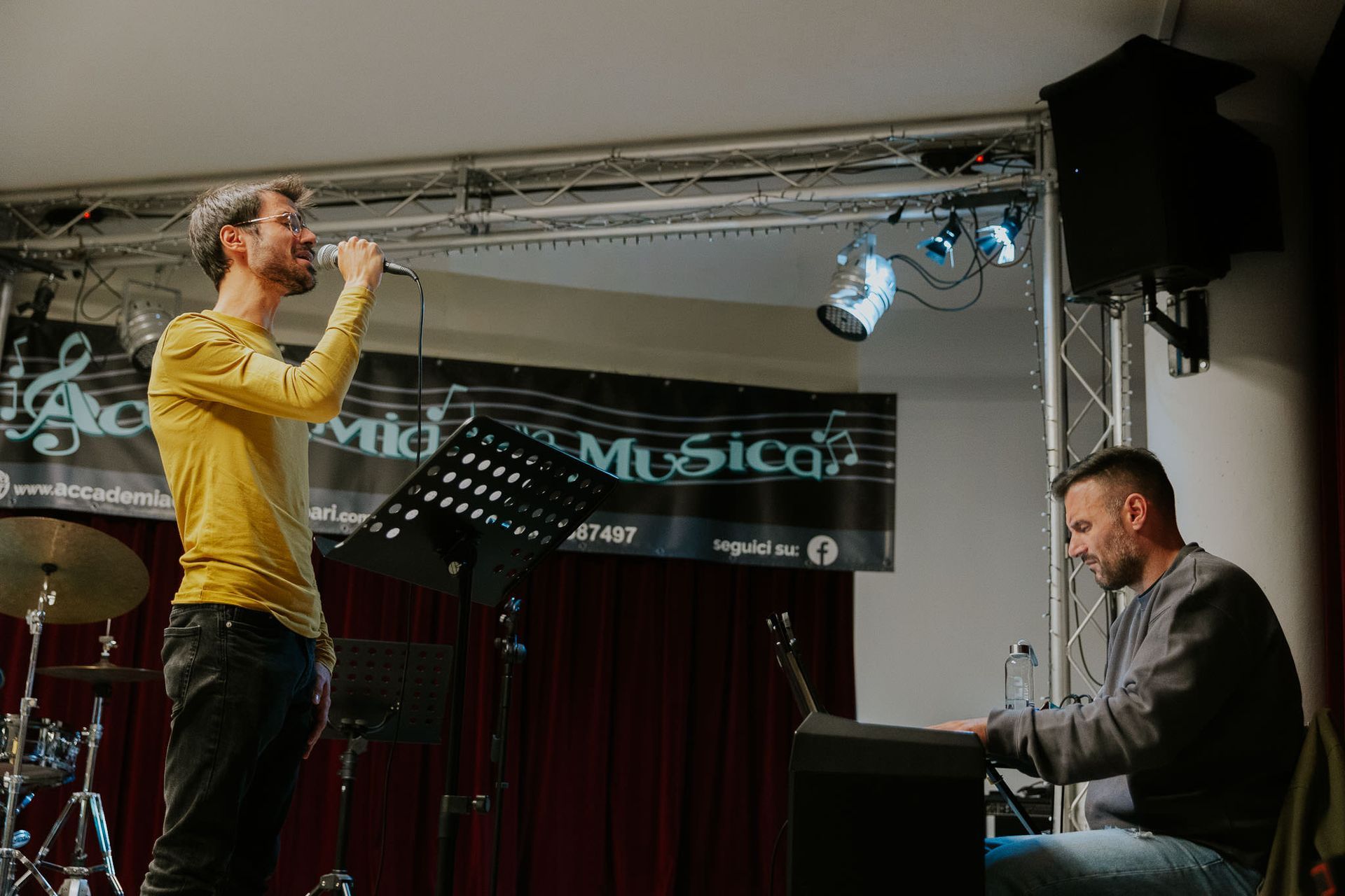 Un uomo canta nel microfono sul palco insieme a un pianista.