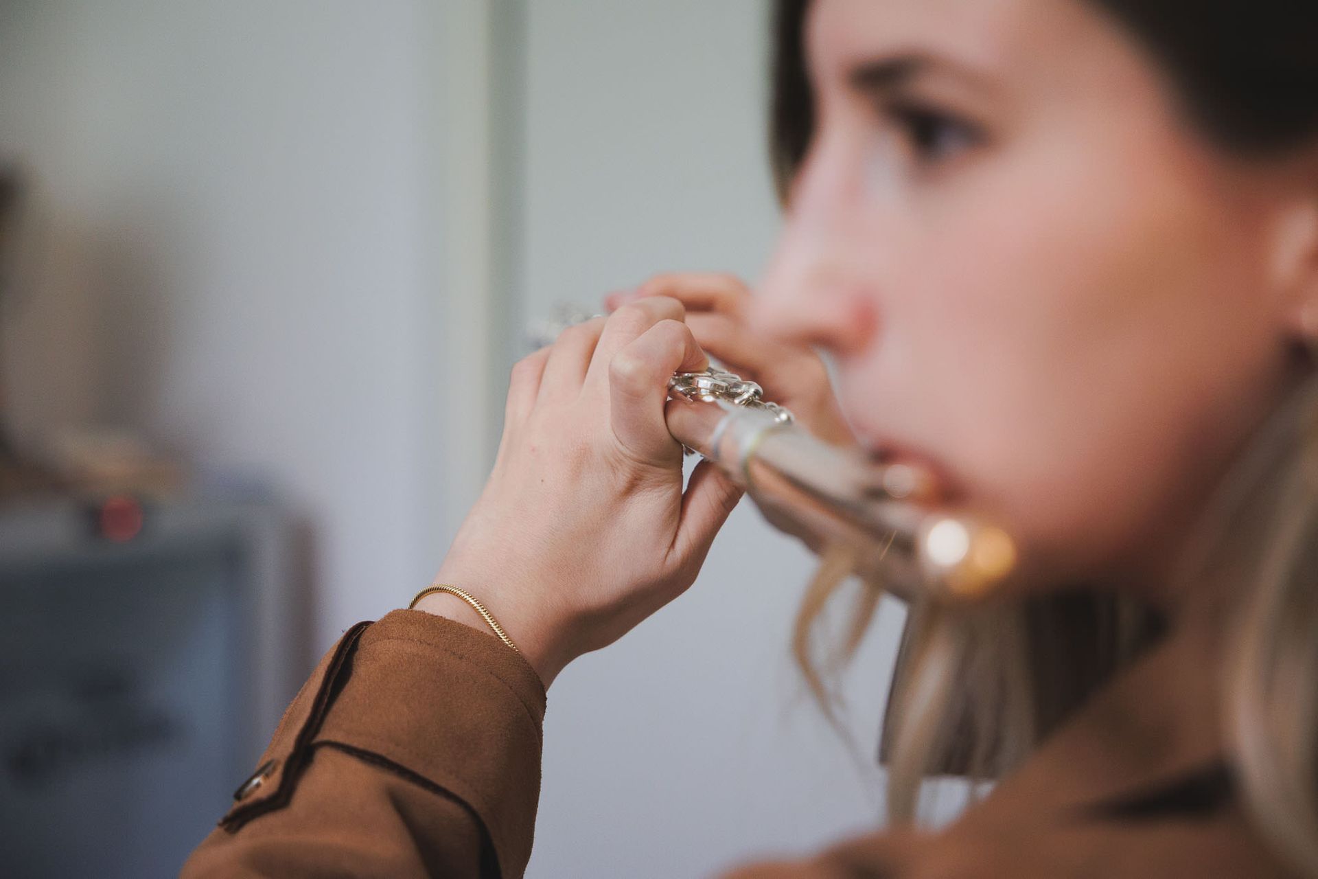 Persona che suona un flauto d'argento, con le mani che tengono le chiavi, giacca marrone.