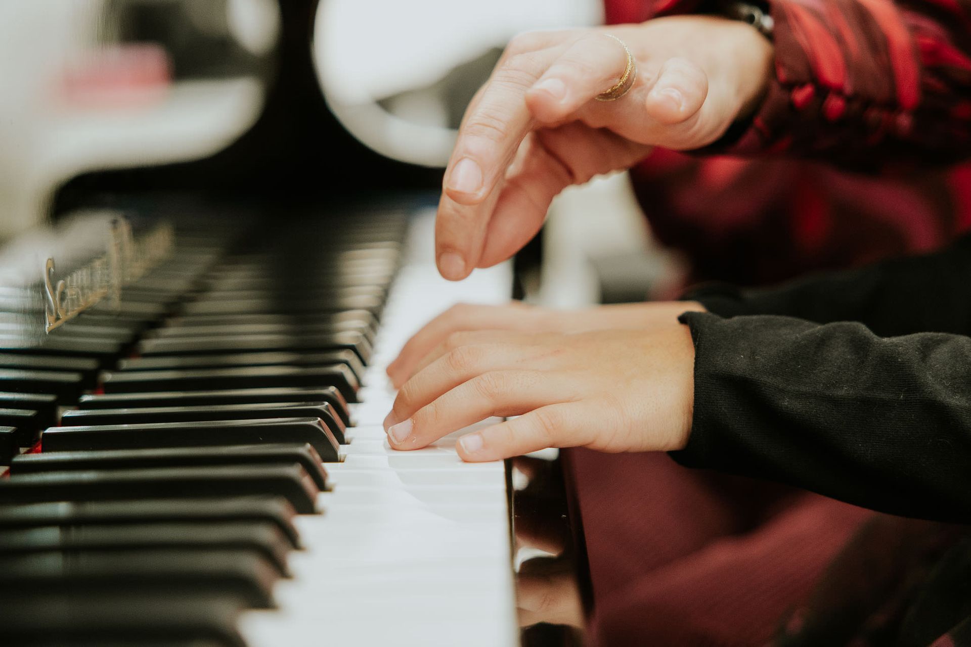 Mani che suonano i tasti del pianoforte; tasti bianchi e neri, giacca scozzese rossa sullo sfondo.