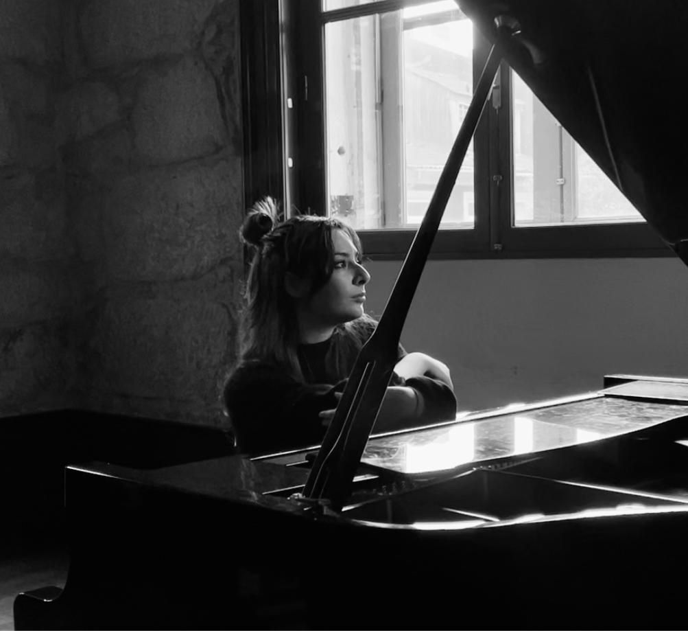 Donna seduta a un pianoforte a coda, con lo sguardo rivolto verso una finestra, ripresa di un interno, in bianco e nero.