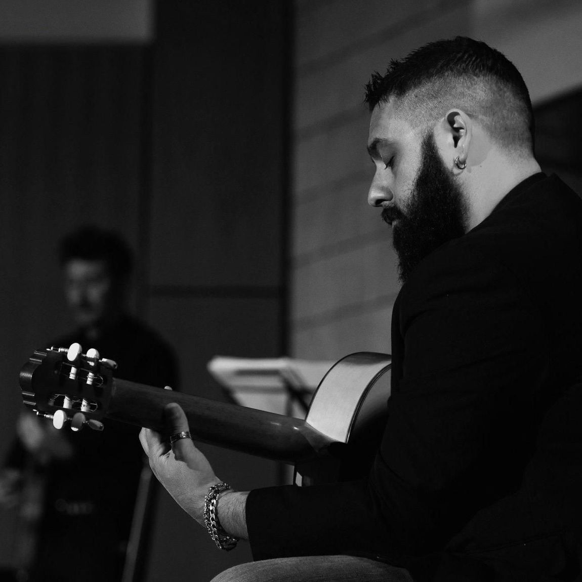Uomo che suona la chitarra acustica, espressione concentrata, scatto in bianco e nero, in interni.