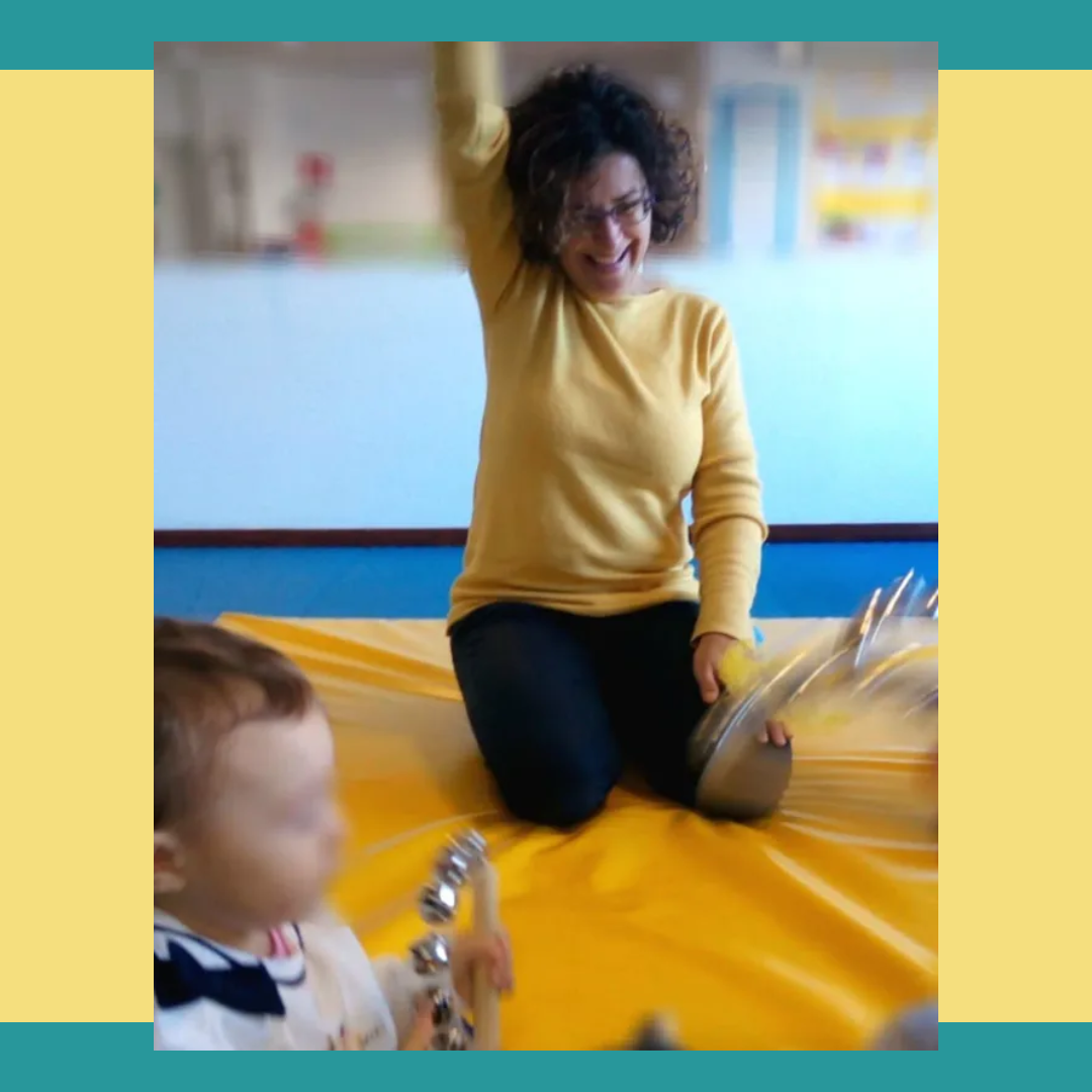 Una donna con i capelli ricci alza il braccio e suona con un bambino su una superficie gialla.