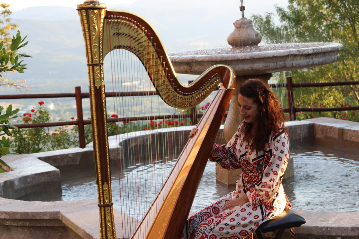 Donna che suona un'arpa dorata vicino a una fontana, all'aperto.