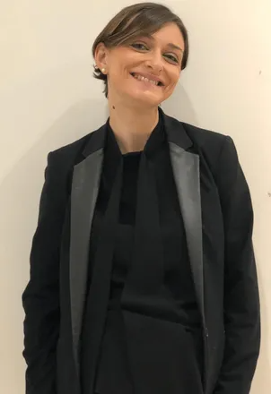 La donna con la giacca nera sorride, guardando avanti.