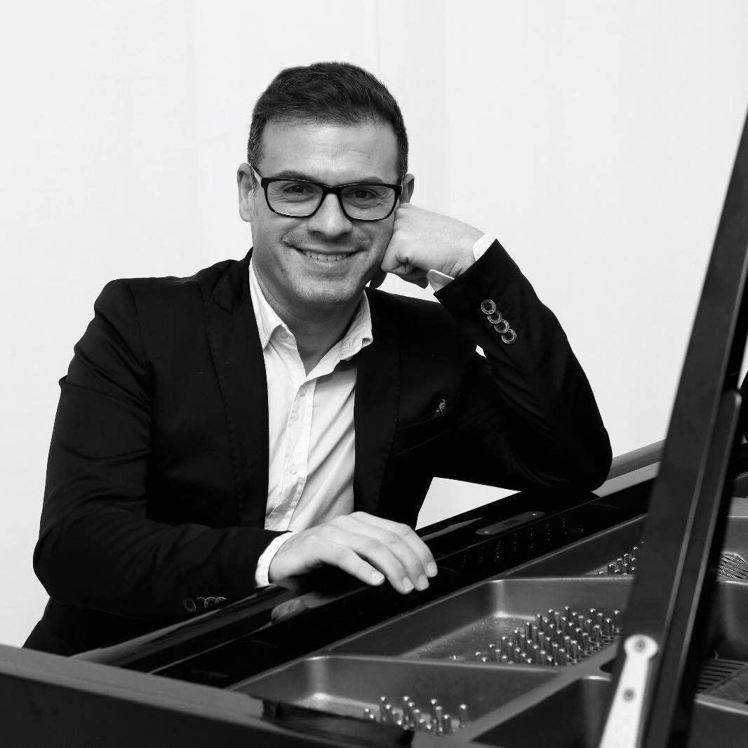 Un uomo con gli occhiali si appoggia al pianoforte e sorride.