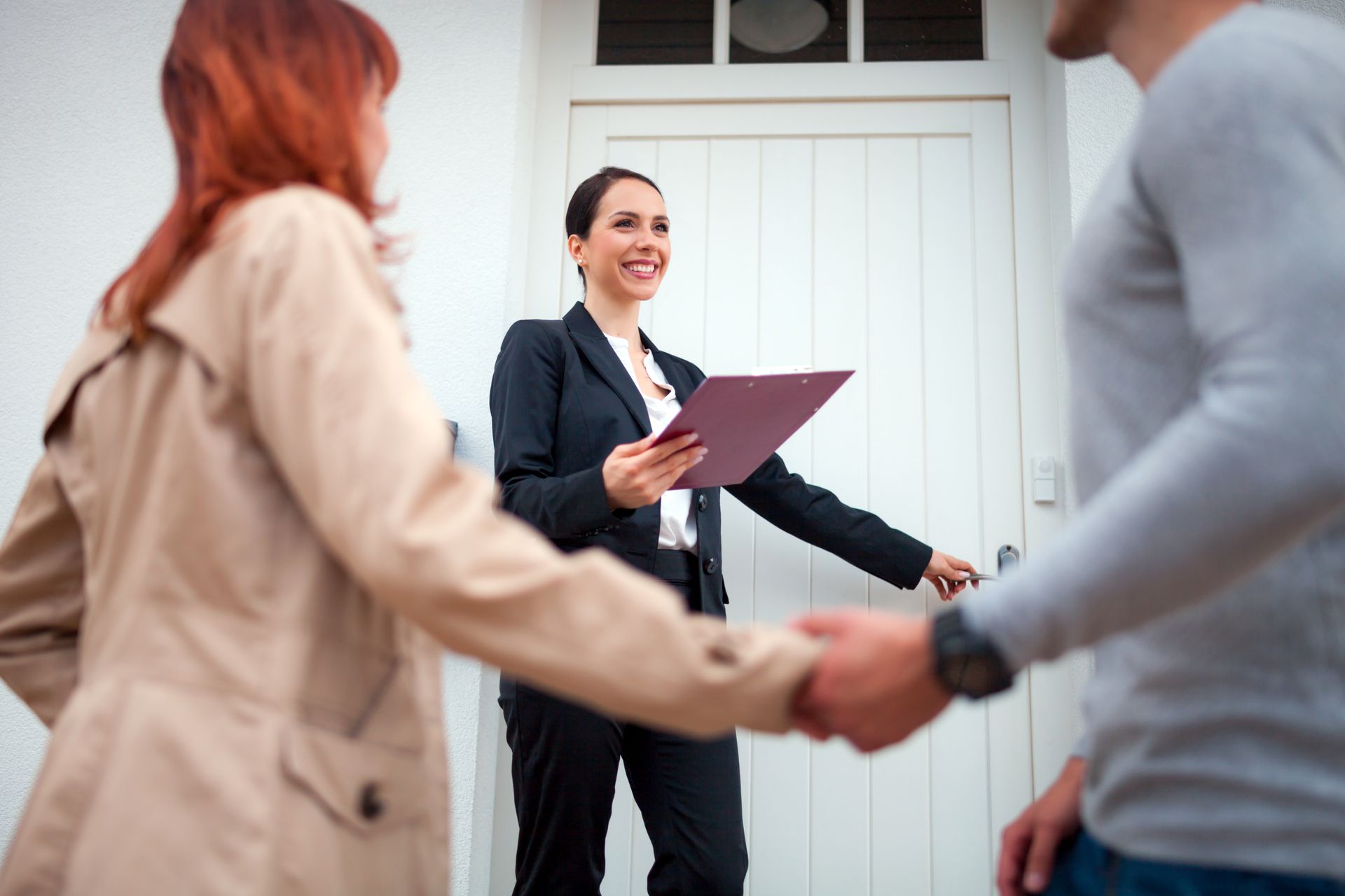 Residential real estate agency agent greeting couple at front door for home showing.
