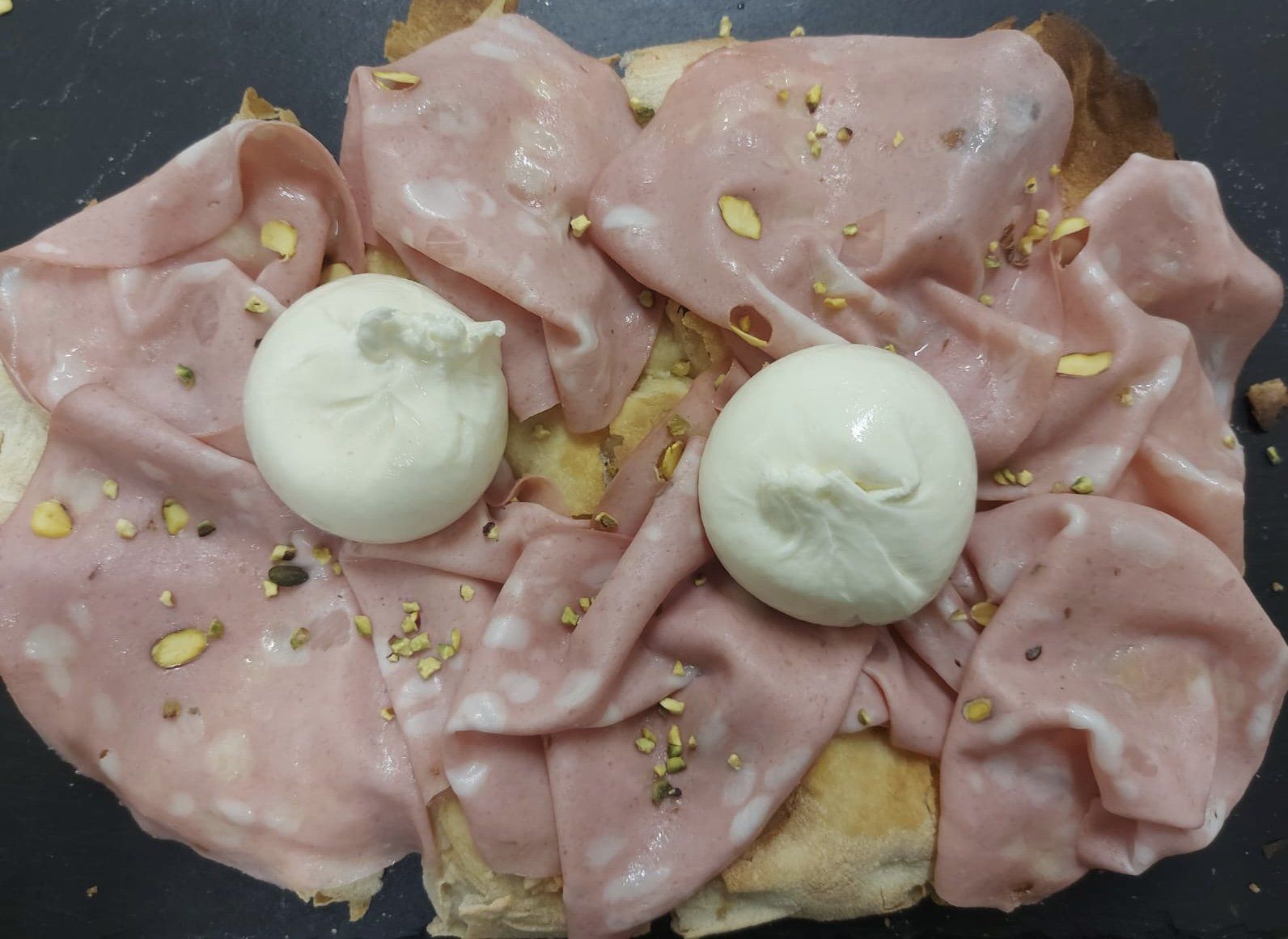 Sandwich aperto farcito con affettati rosa piegati, due palline di mozzarella e spezie sparse.