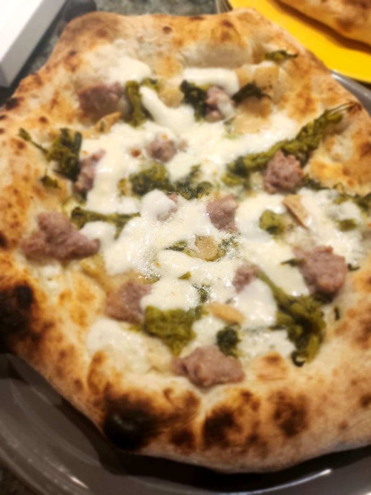 Pizza con formaggio fuso, pesto verde e salsiccia su un piatto scuro