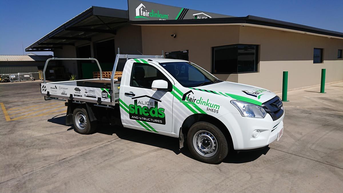A White Truck With The Word Sheds On The Side Is Parked In Front Of A Building — Alice Sheds & Structures In Ciccone, NT