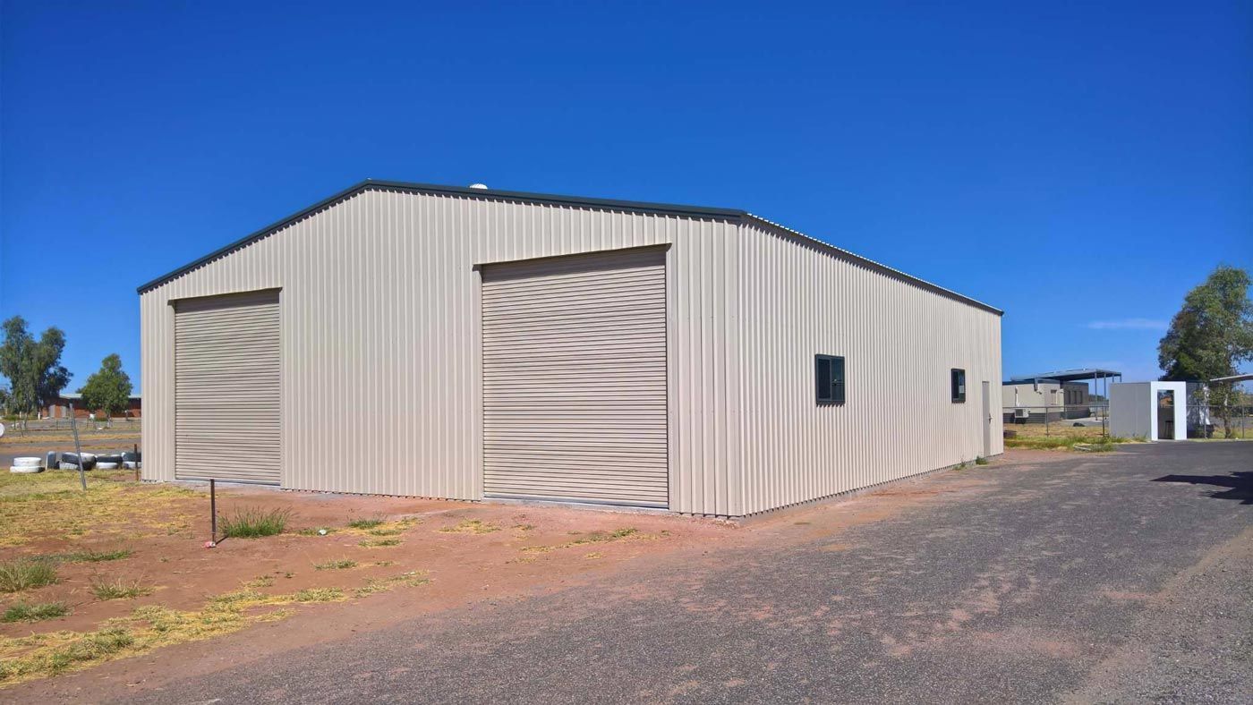 A Large Metal Building With A Garage Door Is Sitting On The Side Of A Road — Alice Sheds & Structures In Ciccone, NT