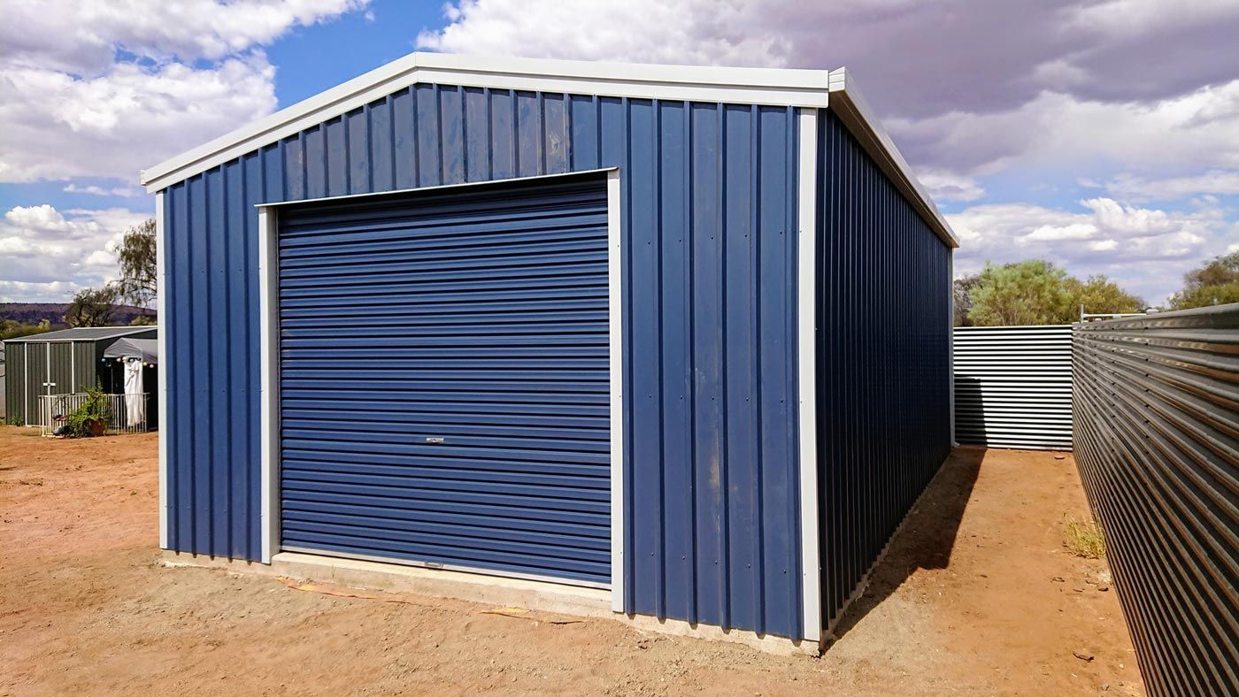 A Blue Garage With A White Trim Is Sitting In The Middle Of A Dirt Field — Alice Sheds & Structures In Ciccone, NT