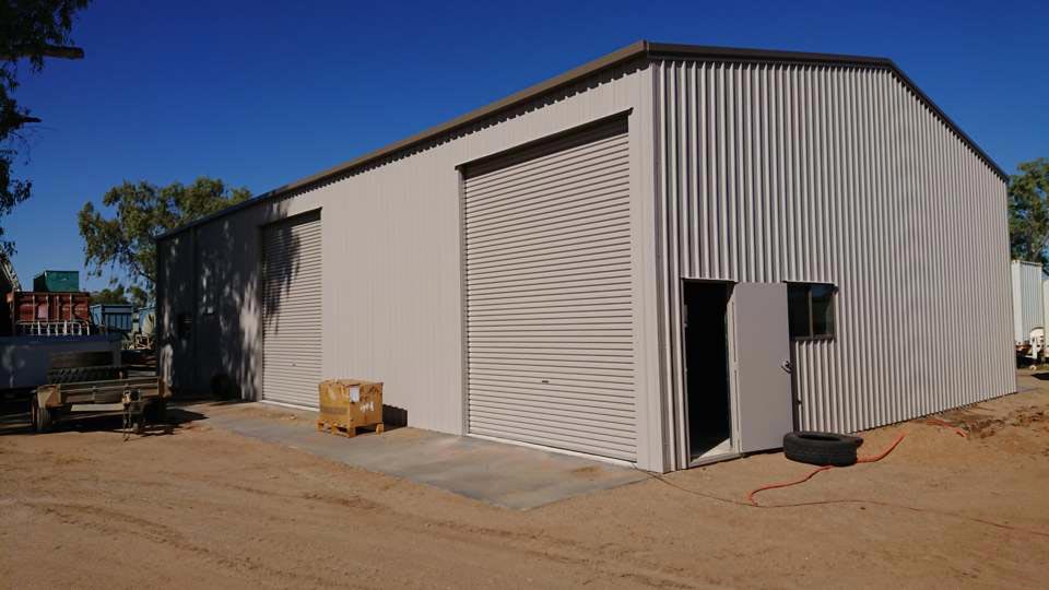 A Large Building With A Garage Door And A Truck Parked In Front Of It — Alice Sheds & Structures In Ciccone, NT