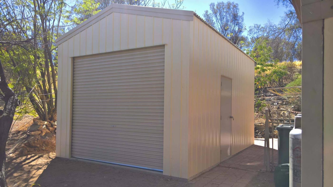 A White Garage With A Roller Door Is Sitting Next To A House — Alice Sheds & Structures In Ciccone, NT