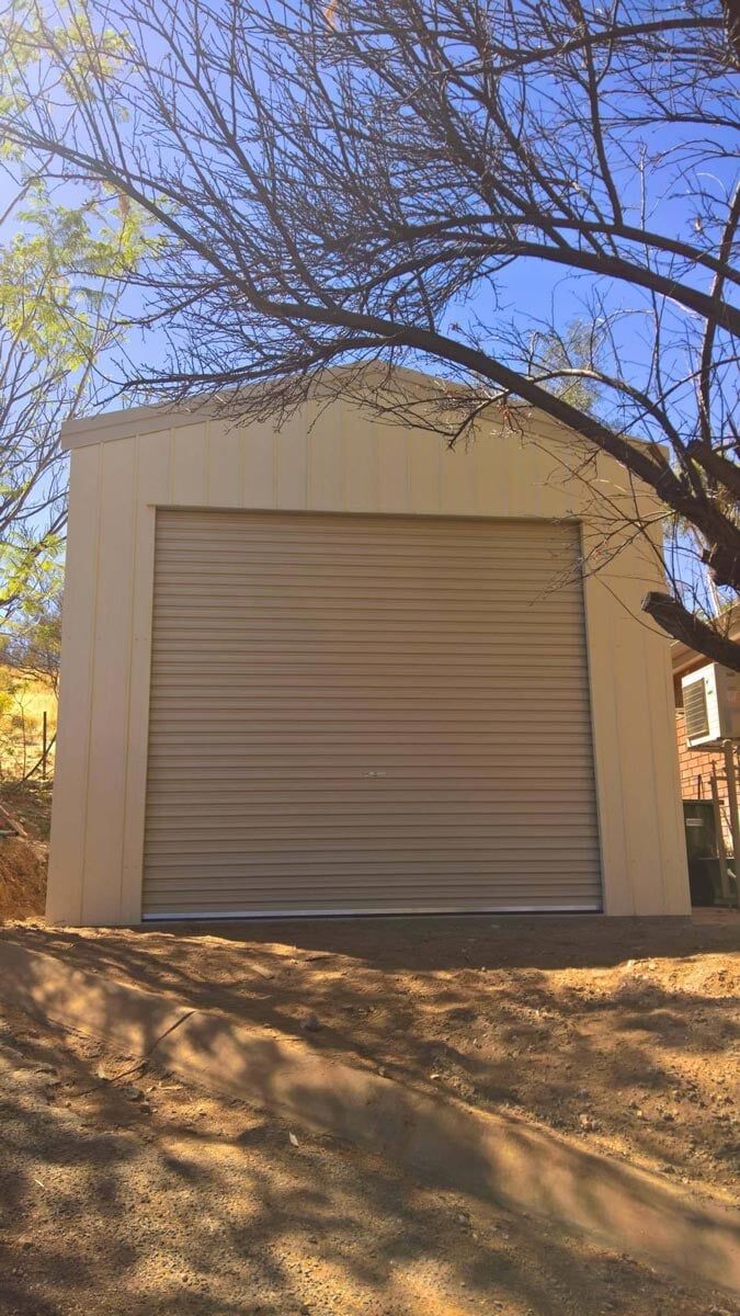 A Garage With A Roll Up Door And A Tree In The Background — Alice Sheds & Structures In Ciccone, NT