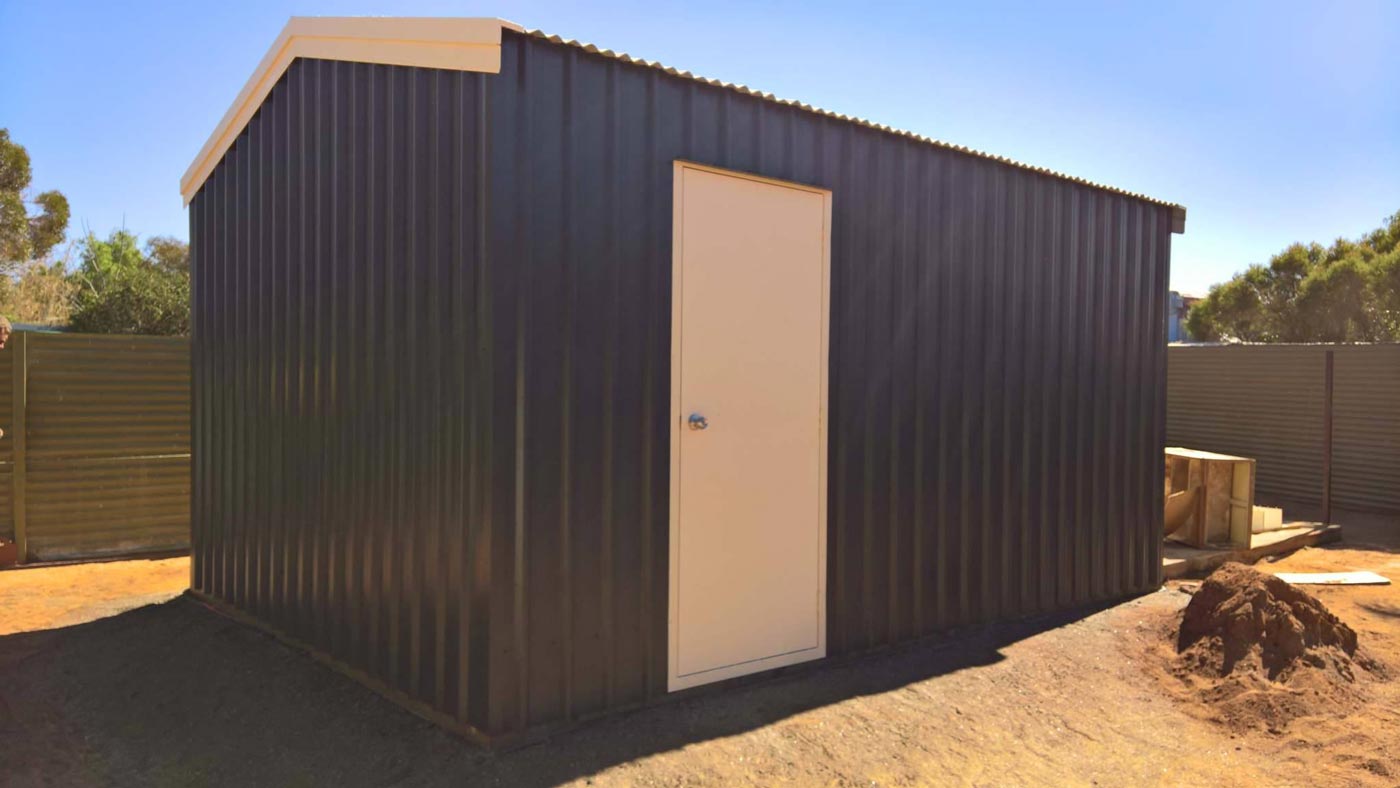 A Black Shed With A White Door Is Sitting In The Dirt — Alice Sheds & Structures In Ciccone, NT