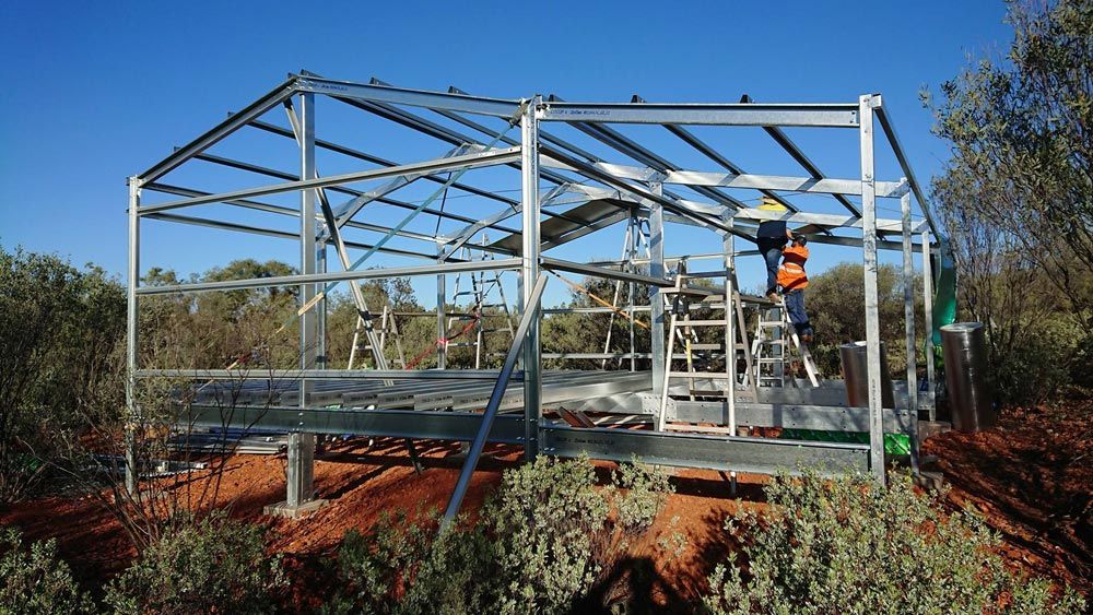 A Man Is Standing On A Ladder In Front Of A Metal Structure — Alice Sheds & Structures In Ciccone, NT