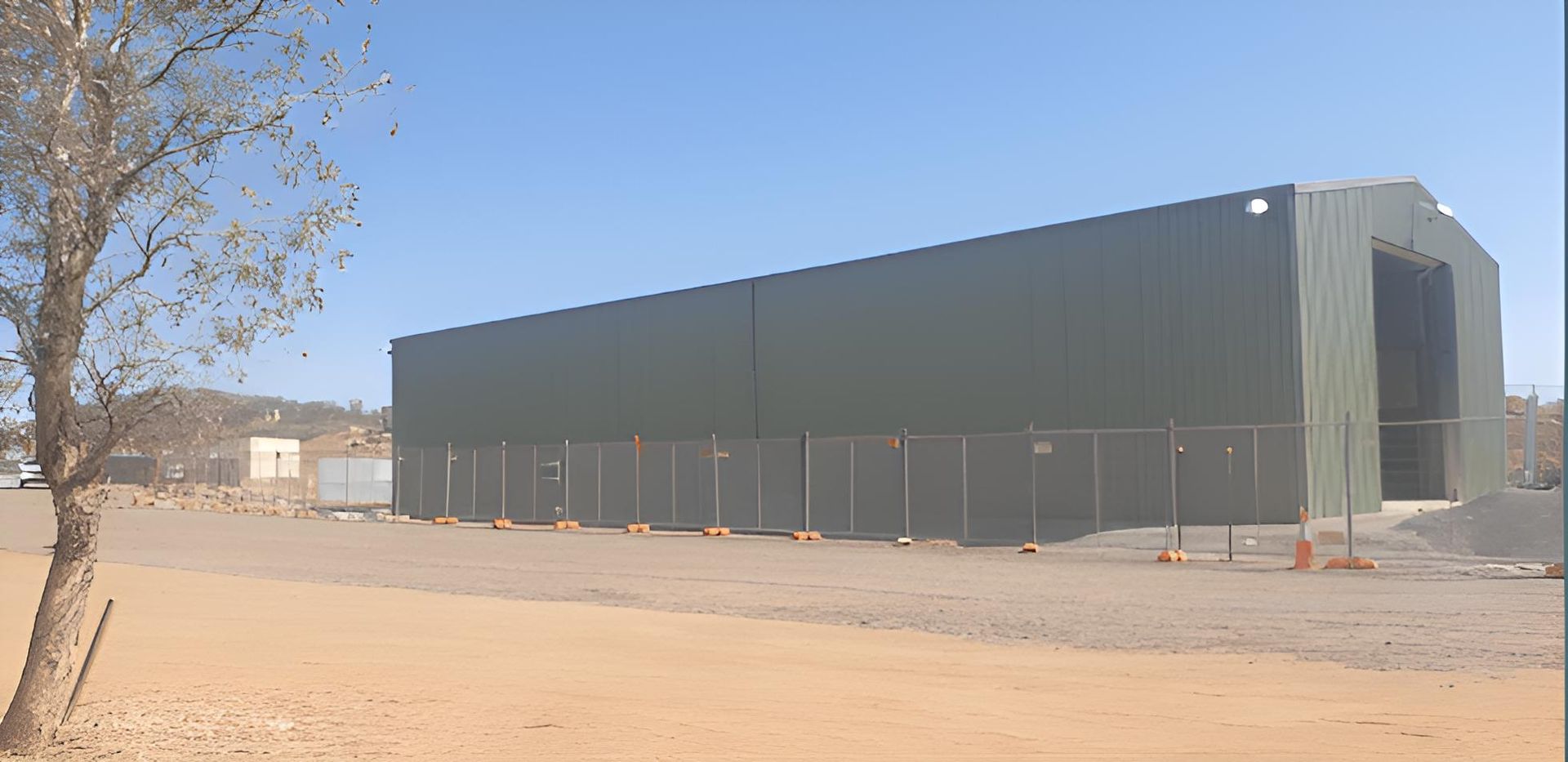 A Large Building With A Fence Around It Is Sitting In The Middle Of A Dirt Field — Alice Sheds & Structures In Ciccone, NT