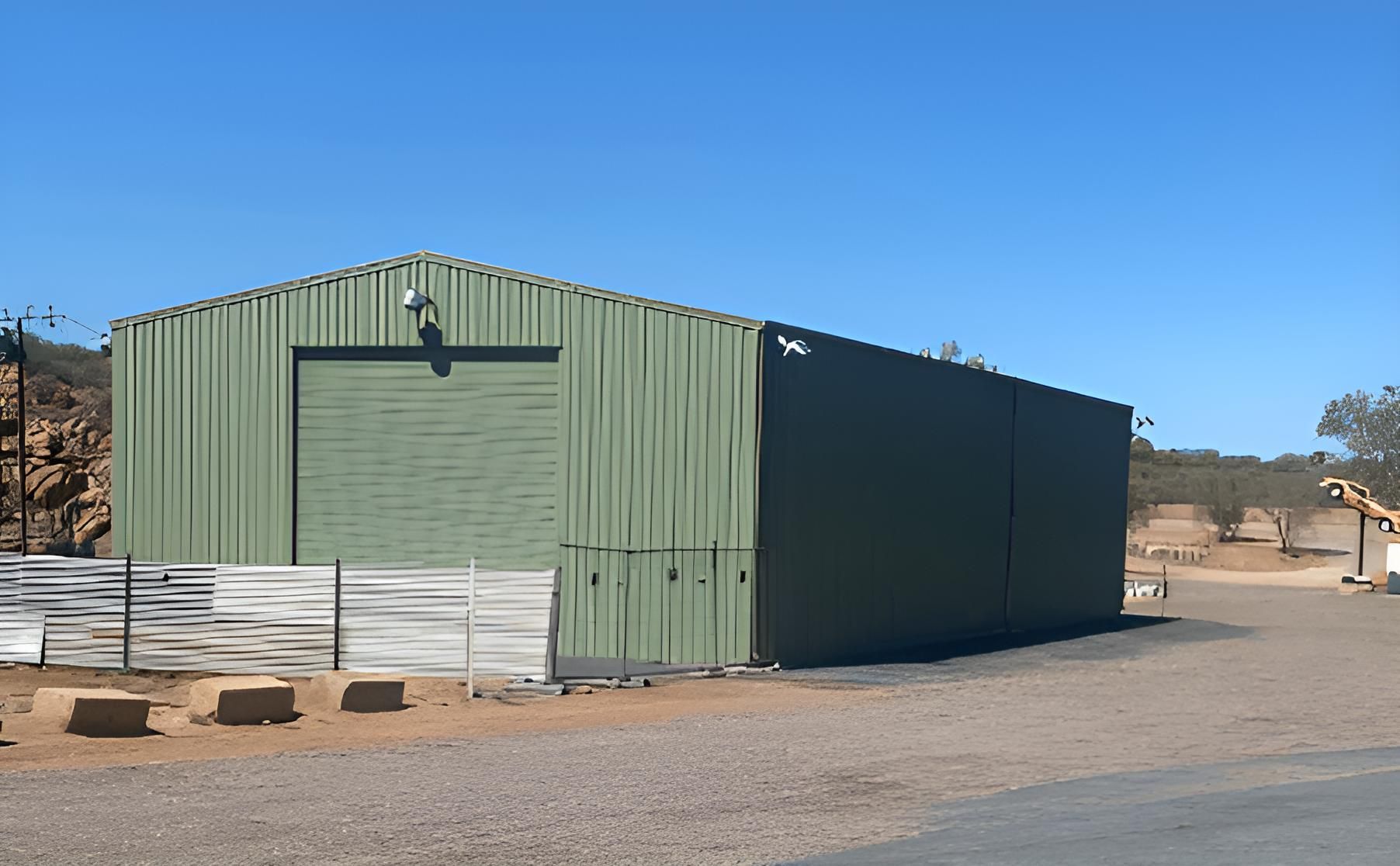A Large Green Building With A Large Garage Door — Alice Sheds & Structures In Ciccone, NT