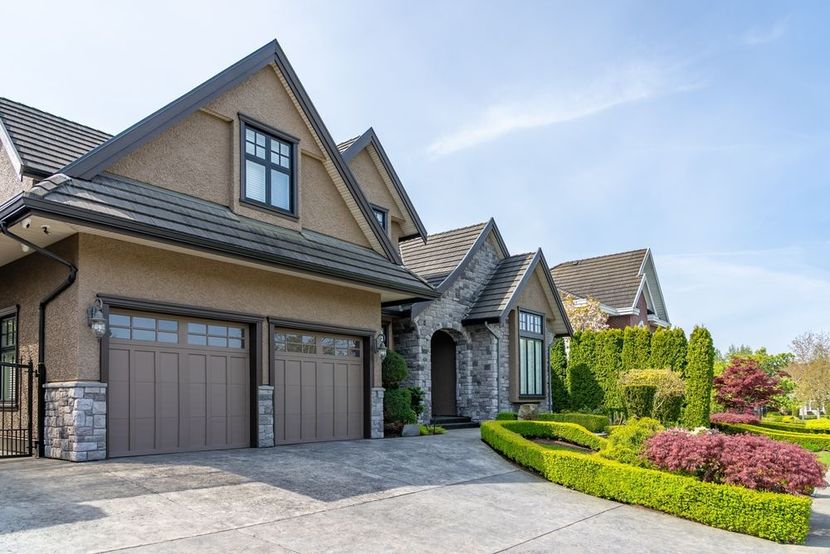 Suburban house with stone entry, double garage, manicured hedges, and a sunlit driveway