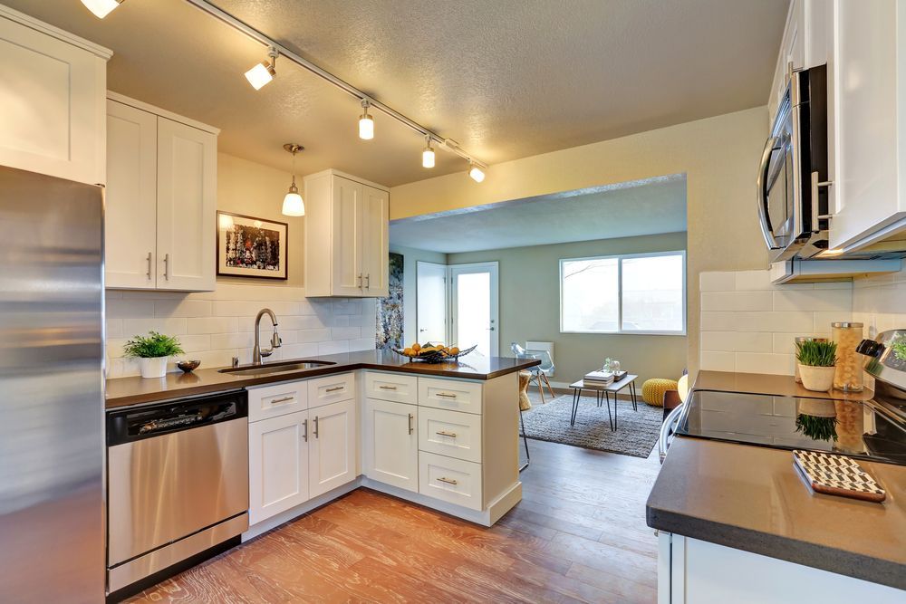 Bright, modern kitchen with white cabinets, stainless appliances, dark countertops, and light wood floors