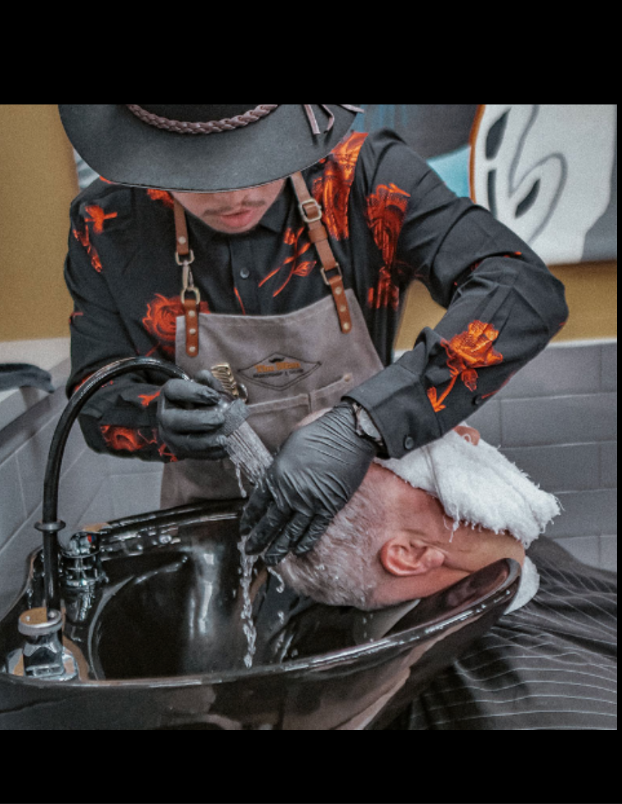 Person washes another's hair in a salon sink. The person washing wears a hat, apron, and gloves.